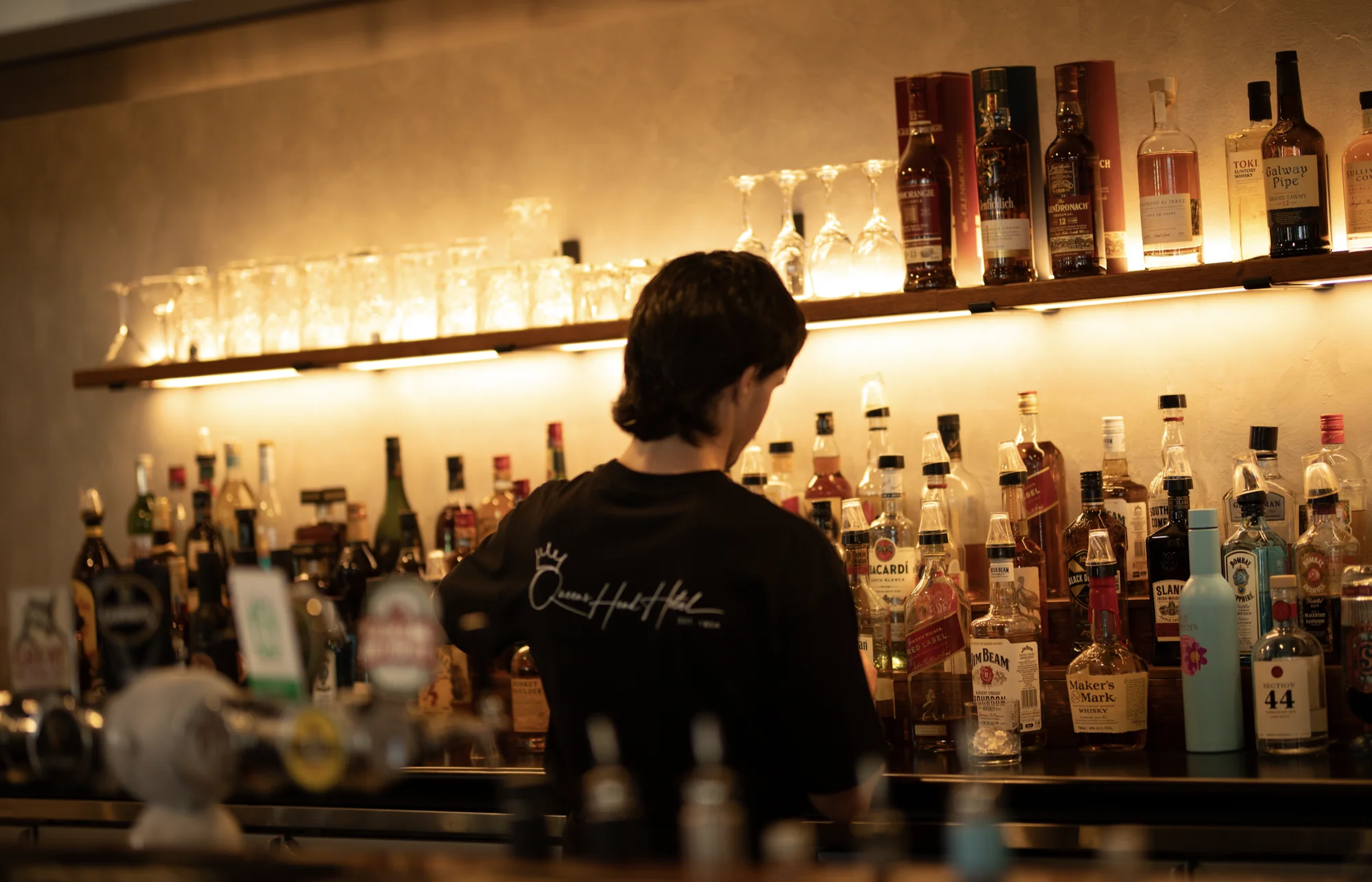 A Queen’s Head team member behind the warmly lit bar